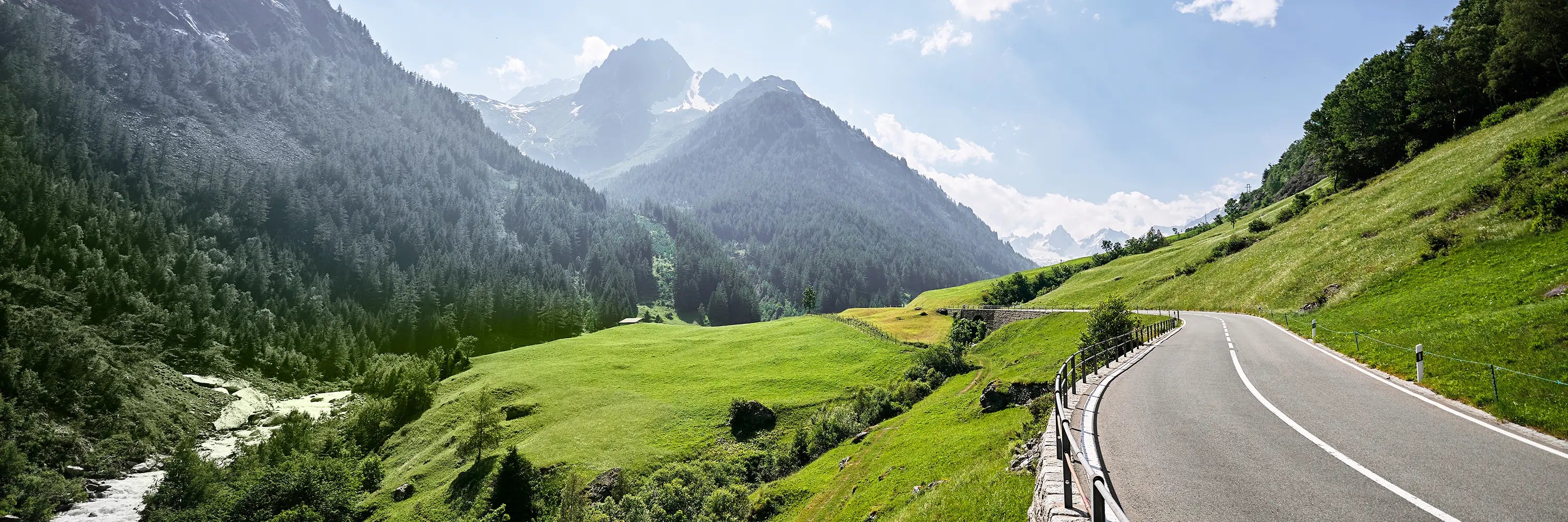 Eine kurvenreiche Straße durch eine malerische Berglandschaft mit viel Grün und klarem Himmel.