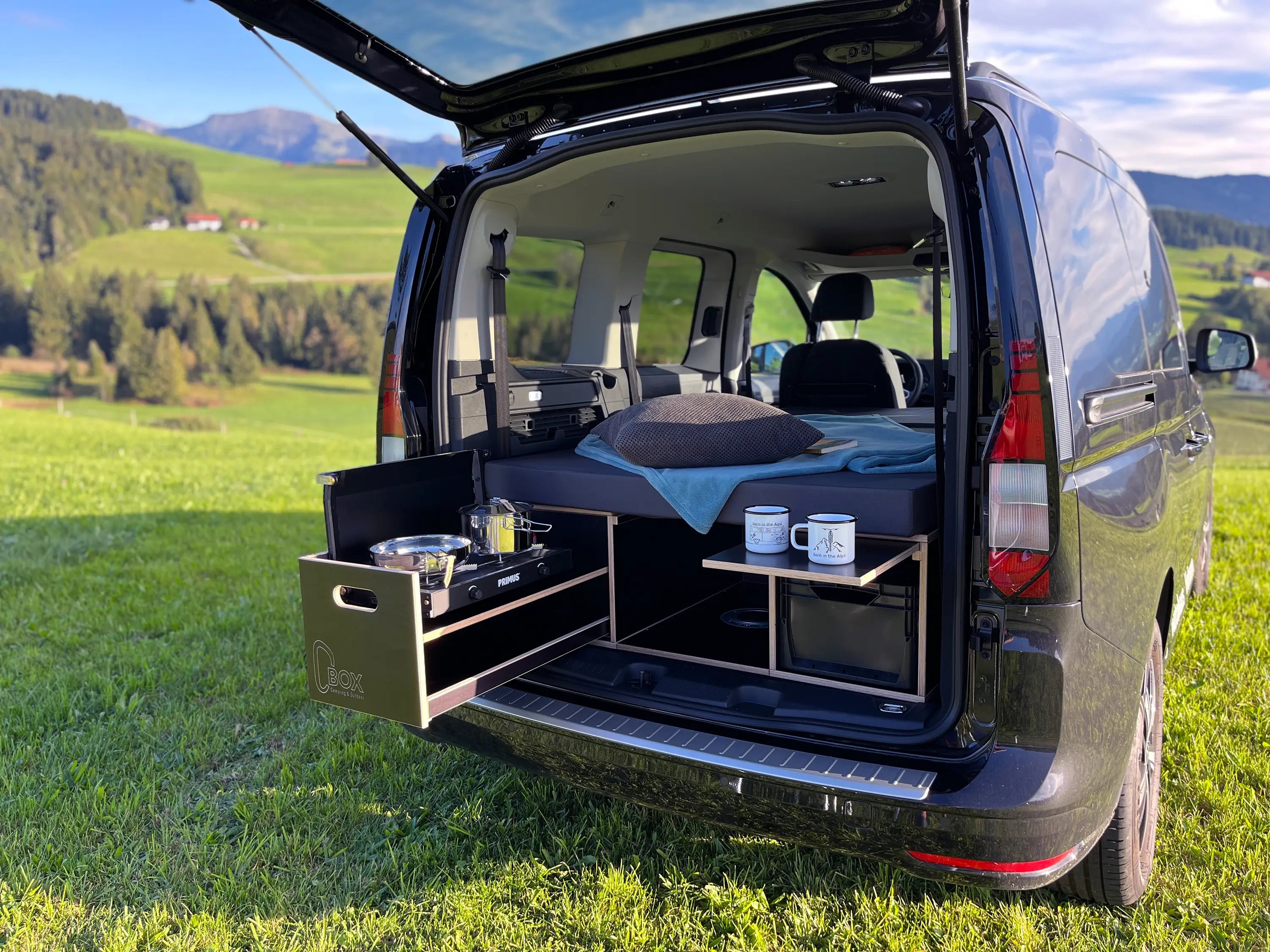 Van mit offenem Kofferraum, der eine Campingbox in einer malerischen Umgebung im Freien zeigt